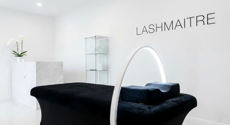 Interior of a luxury lash studio featuring a sleek white Half Moon eyelash extension light arching over a black velvet lash bed, casting a bright, shadowless glow. LASHMAITRE professional equipment.
