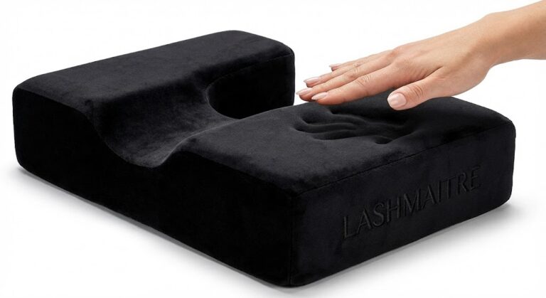 Side view of a black velvet eyelash extension pillow by LASHMAITRE, with a hand pressing into the memory foam to demonstrate high density and ergonomic support