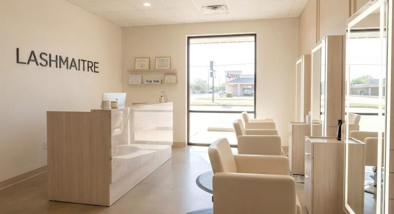 Interior photograph of the modern and luxurious LASHMAITRE studio, known as the best lash salon in Tyler, Texas, featuring a marble reception desk, bright styling stations, and framed certificates.
