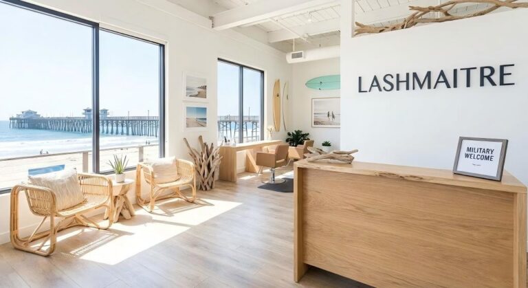 The interior of LASHMAITRE, a salon specializing in eyelash extensions Oceanside, featuring bright beach decor, a "Military Welcome" sign on the reception desk, and large windows overlooking the Oceanside Pier and ocean.