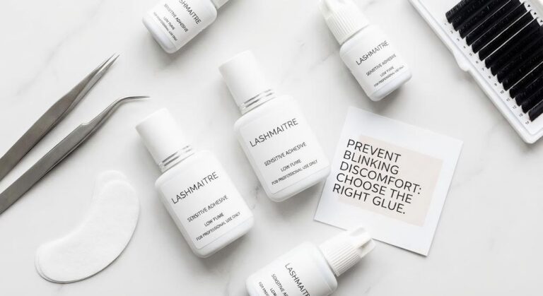 A flat lay display of professional LASHMAITRE lash extension adhesive bottles, highlighting the importance of high-quality glue in preventing the issue where eyelash extensions hurt when I blink.