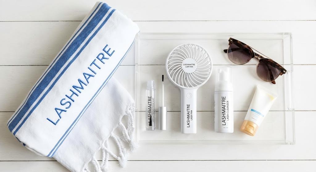 A flat-lay photograph of the LASHMAITRE Swim Proof Lash Kit, featuring a branded towel, protective sealant, cleanser, and mini fan, providing the essential products to answer the question: with eyelash extensions can you swim safely?