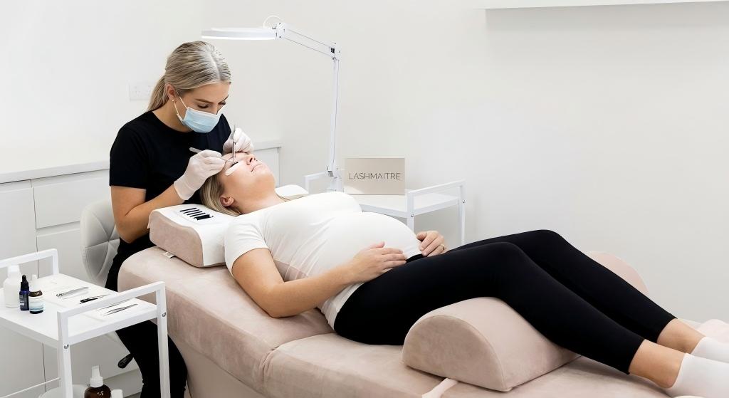 A professional lash artist applying extensions to a pregnant client positioned at a 45-degree angle, demonstrating the correct modification to ensure Safe Eyelash Extensions for Pregnant Clients Lying on Their Back.