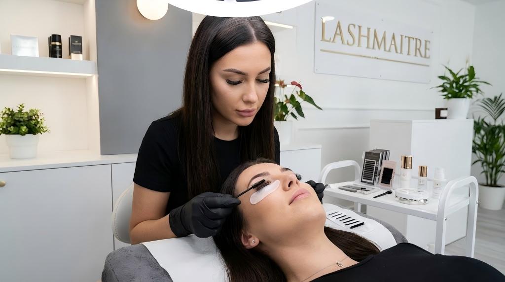 Professional lash artist applying safe, water-based mascara on eyelash extensions with a disposable wand at LASHMAITRE salon.