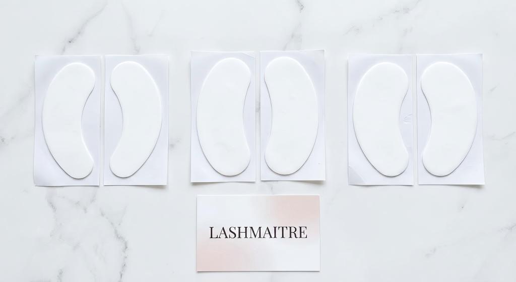 Display of banana, oval, and kidney-shaped eye patches for eyelash extensions laid out on a white surface next to a Lashmaitre brand card.
