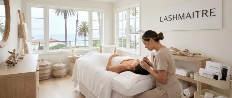 A professional lash artist applying extensions in a bright, sunlit studio with coastal decor elements, demonstrating the premium quality of LASHMAITRE wholesale eyelash extensions in Santa Barbara.