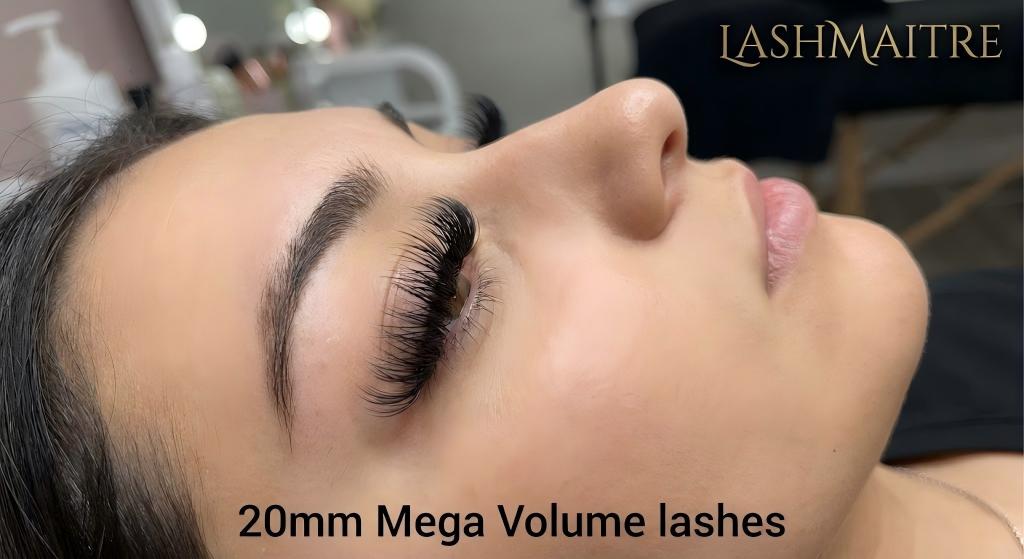 A side profile view of a woman with her eyes closed, demonstrating the LASHMAITRE 20mm Mega Volume lashes, which are the longest eyelash extensions applied safely. The dark, dense lashes curl upwards, showing the dramatic length and volume.
