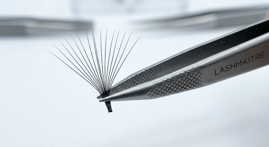 Extreme macro photography of a diamond-etched inner boot of extension eyelash tweezers securely gripping a 15D Mega-Volume fan without base separation under clinical laboratory lighting.